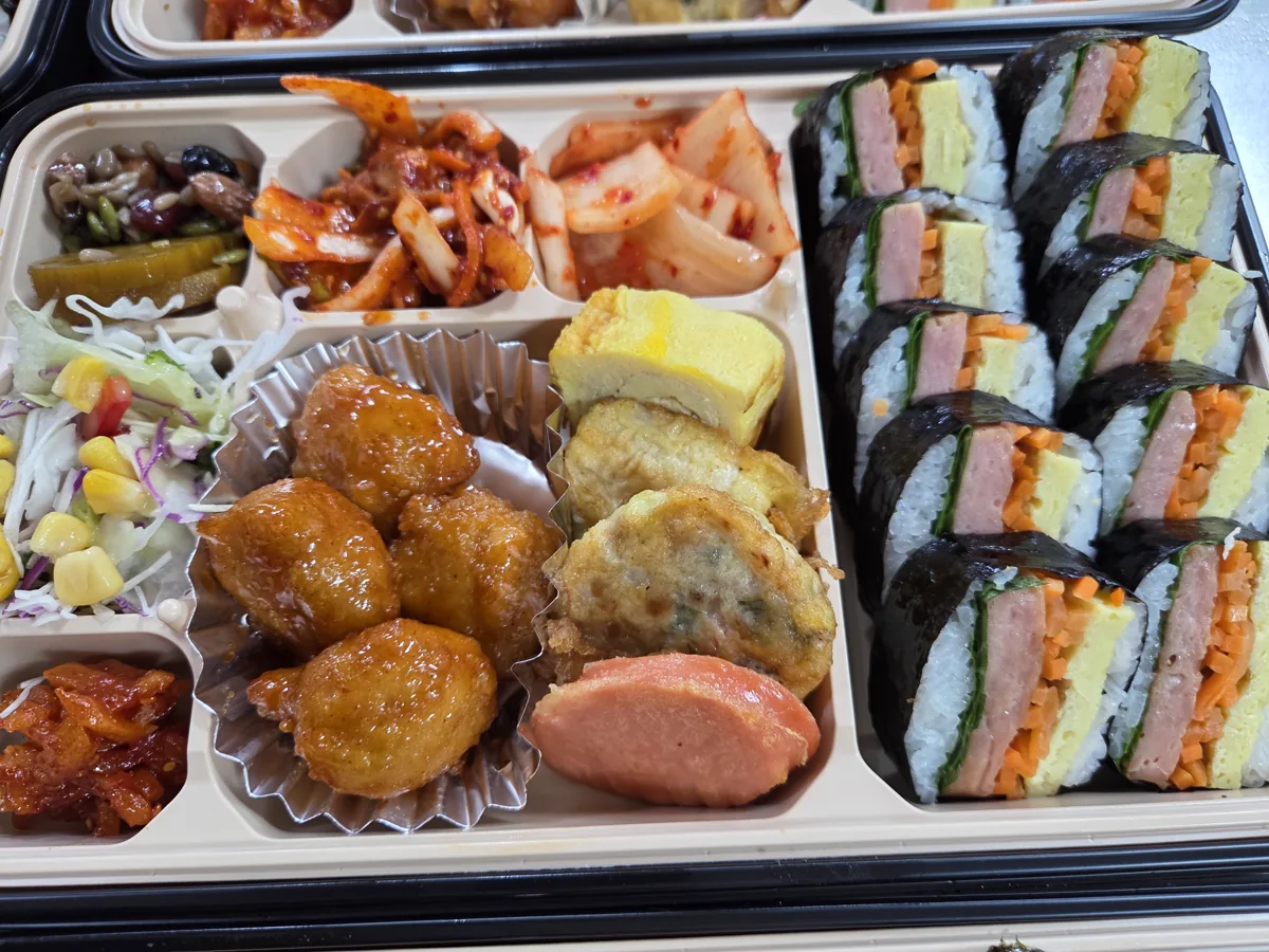 김밥과 달걀말이, 전, 샐러드, 김치와 여러 반찬을 한 용기에 담은 실제 단체도시락